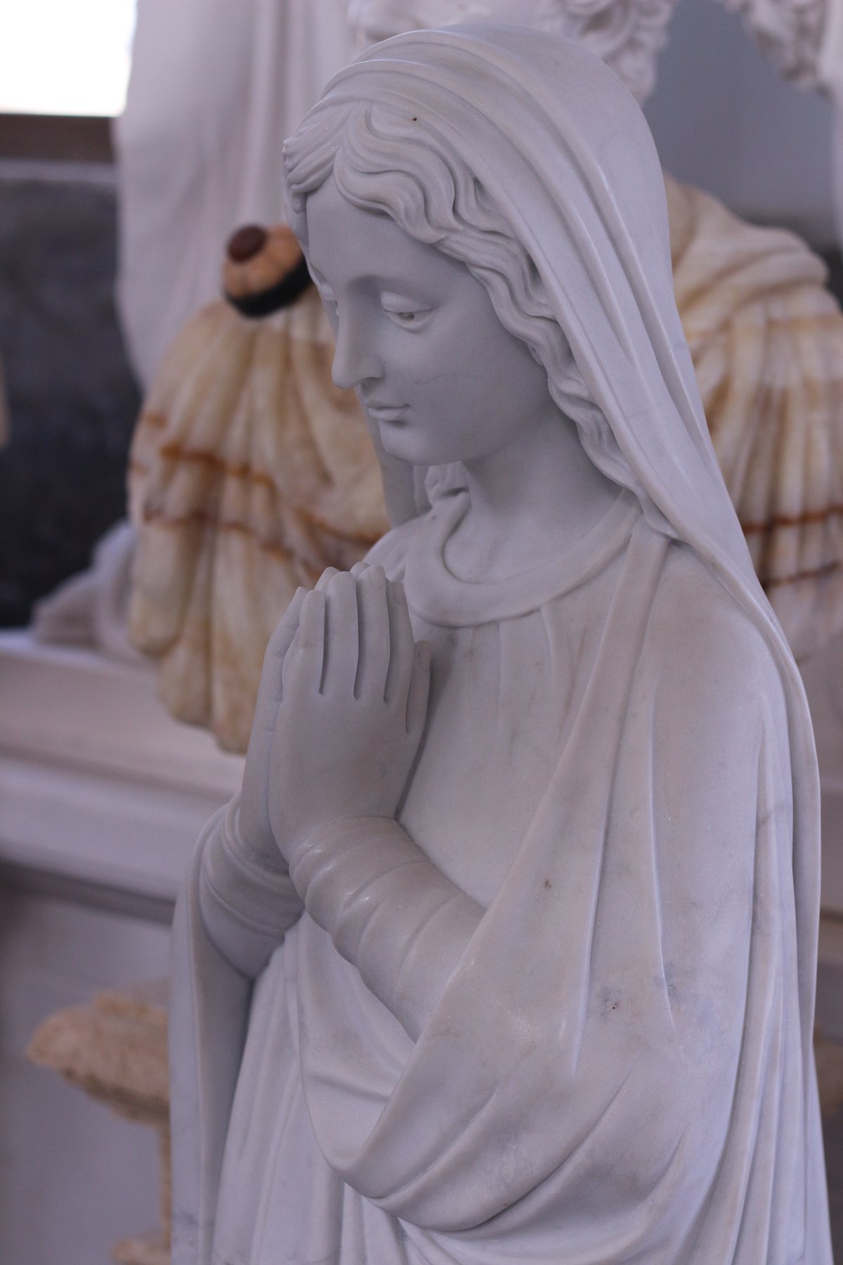Marble figure in a veil with hands clasped in prayer, showing fine carved drapery