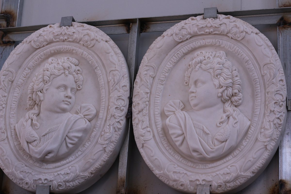 Two oval carved medallions with female portrait busts, seen in the workshop